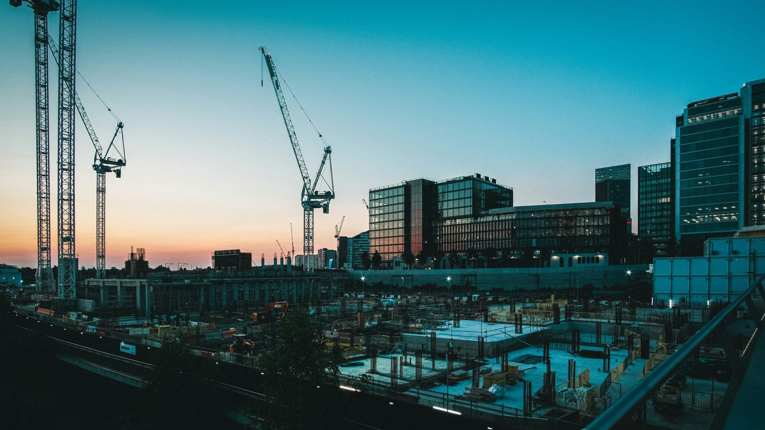 Construction site with tower cranes and city skyline at dusk